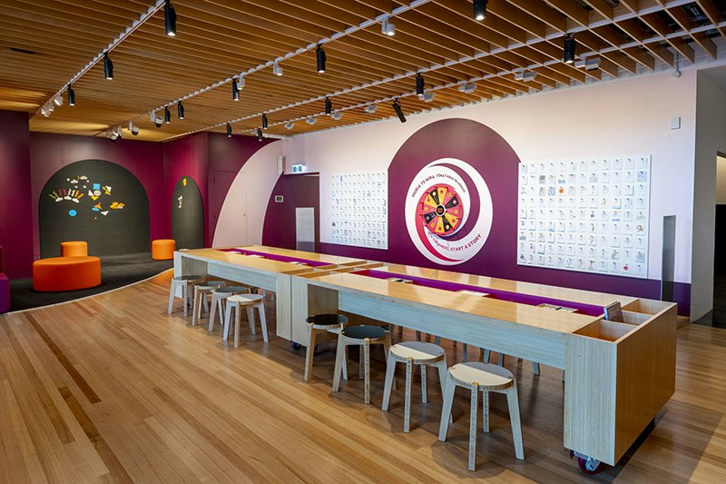 Brightly coloured space with long tables and stools in the middle
