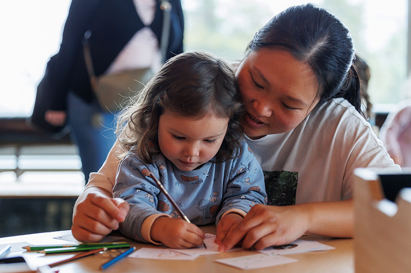 An adult and child working at a table with coloured pencils and paper.