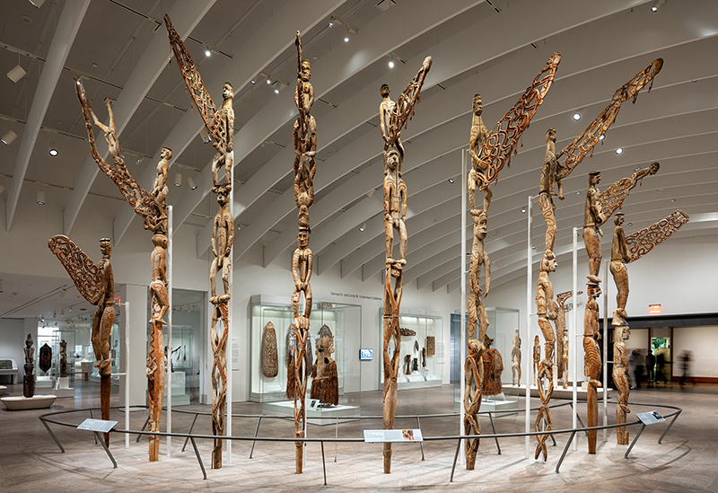 An installation of several tall carved poles in a gallery.