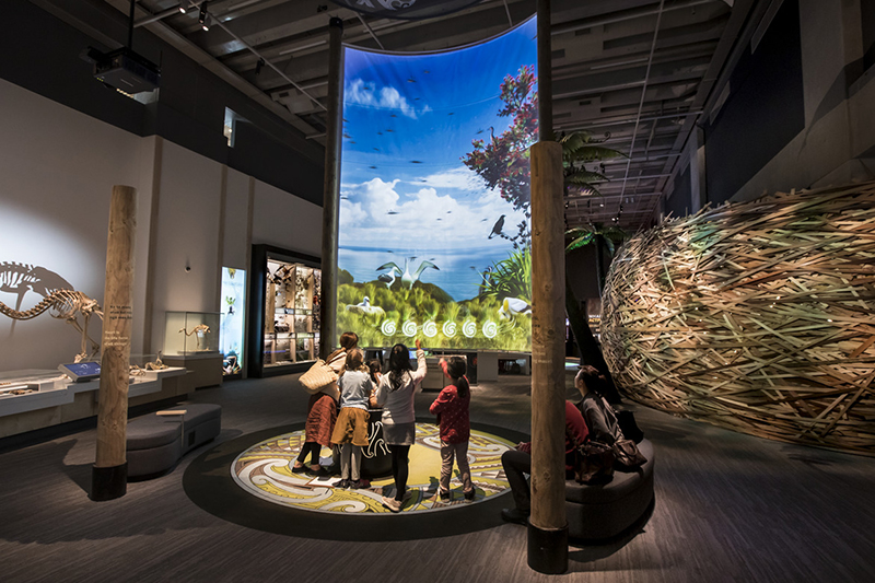 Children in front of a large convex screen with a photo of nature on it. They are in a museum room.