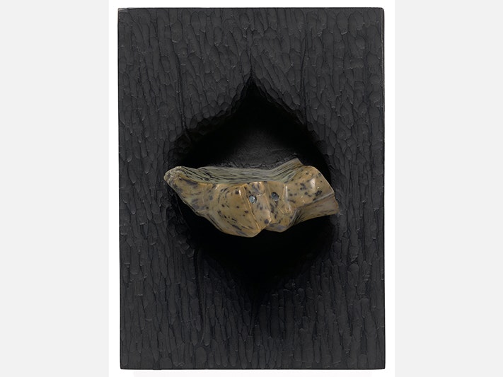 Fred Graham CNZM, Ohorere, 1984.Purchased 1988 with New Zealand Lottery Board funds. Te Papa (1988-0013-1) A photograph of a sculptured piece of stained kauri and nephrite on a dark wall.
