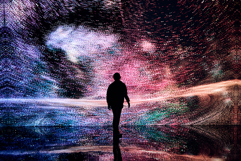 A silhouette of a person standing in front of a large screen of a digital light display which is also reflected on the floor.