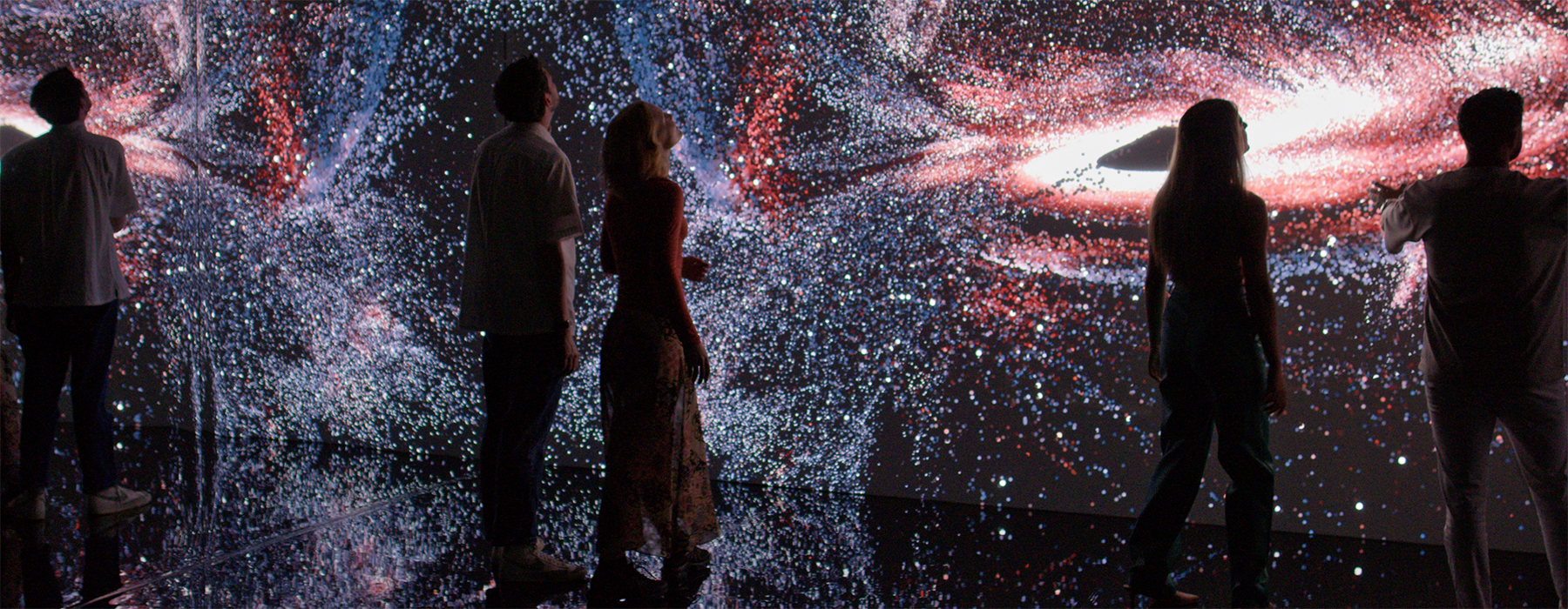 Several people are standing in front of a digital screen with light patterns showing on it.