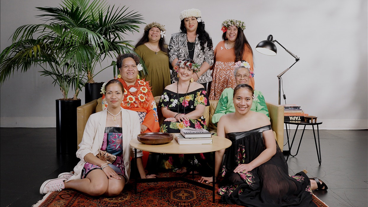 Eight women arranged around a sofa on a stage and smiling at the camera.