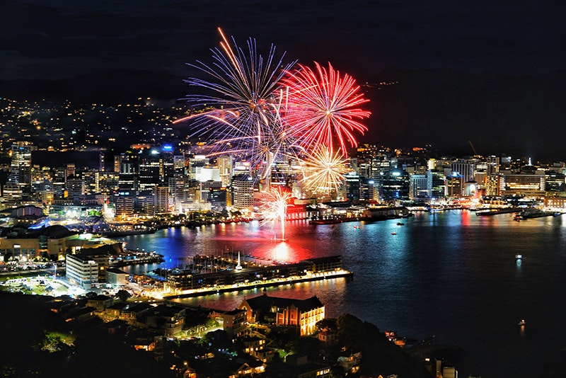 A night-time photograph of Wellington city with large fireworks exploding over the harbour.