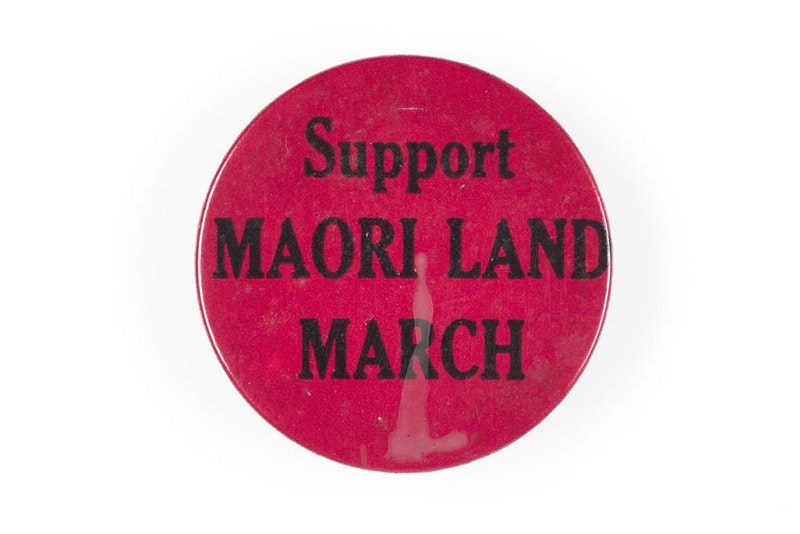 A dark pink badge with the words Support Māori Land March.