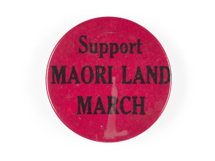 Support Maori Land March badge, maker unknown. Gift of Meg Bailey, 2020. Te Papa (GH025627) A dark pink badge with the words Support Māori Land March.