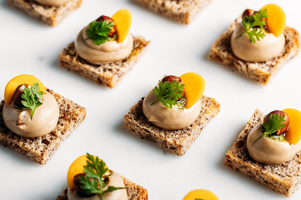 Small canapés with a mousse and piece of fruit and a green herb on each one.