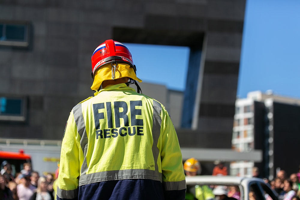The back of a fire service person with a high-vis Fire rescue coat and hat on.
