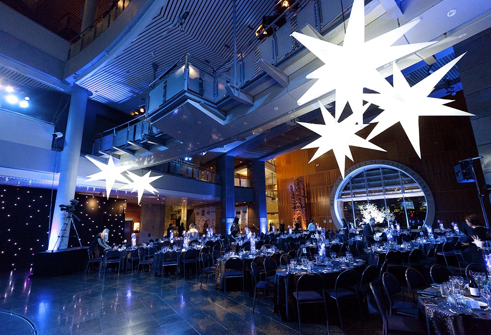 A large gallery space at Te Papa set out with tables and chairs and giant white stars hanging from the roof.