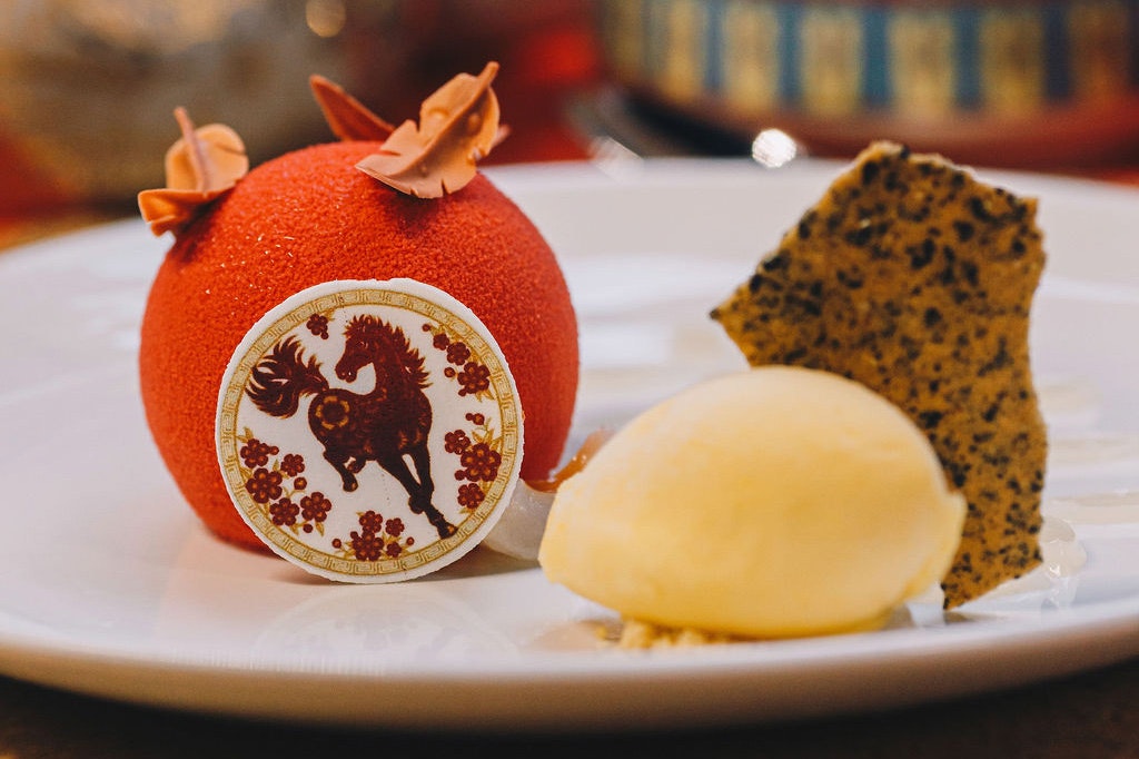 A plate of dessert with some ice cream, cake and a themed orange ball with a horse on it.