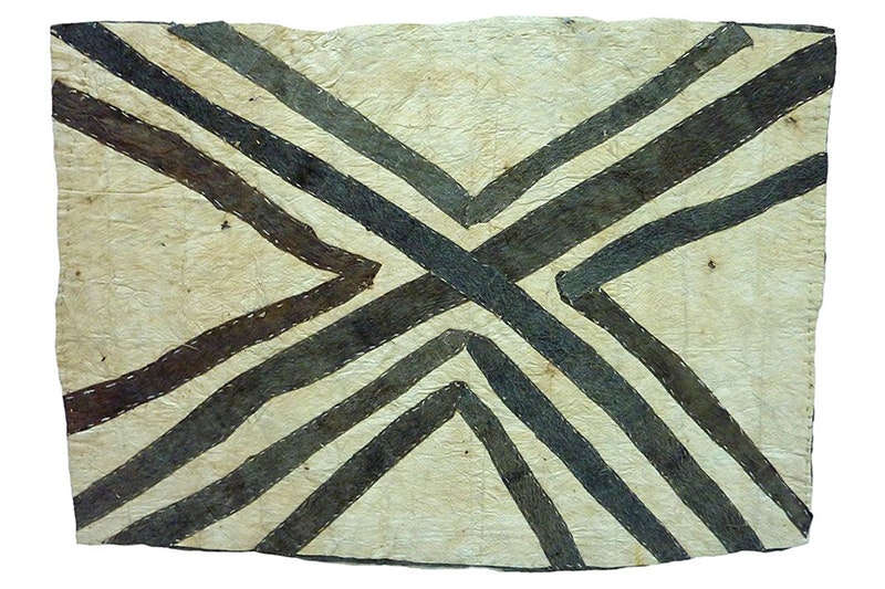 A piece of tapa cloth with a large X painted across it with extra lines either side of the main X.