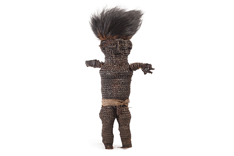 A small doll with hair sticking up made from feathers and plant fibres on a white background.