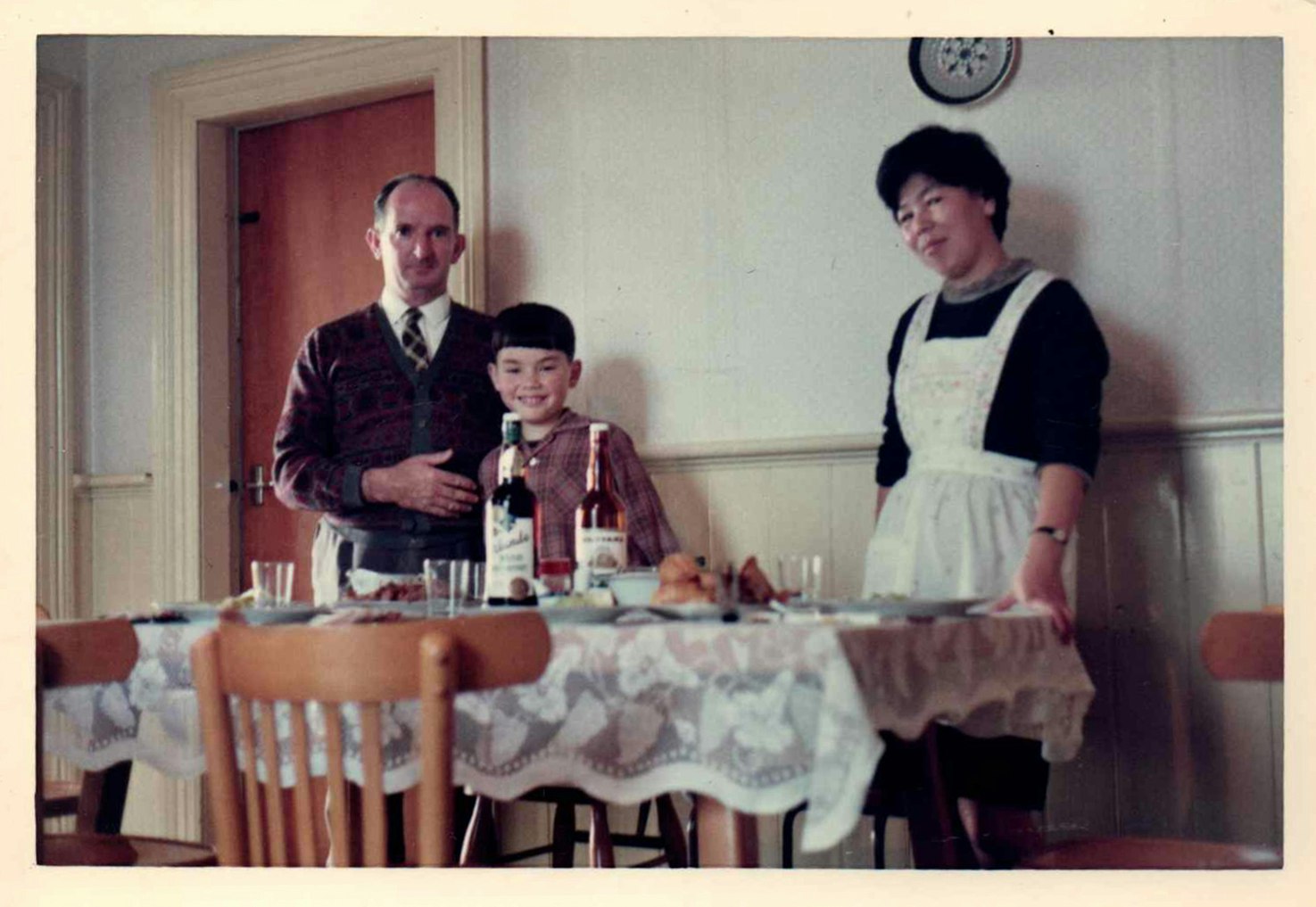 A father, mother and child are posing behind a dining table.
