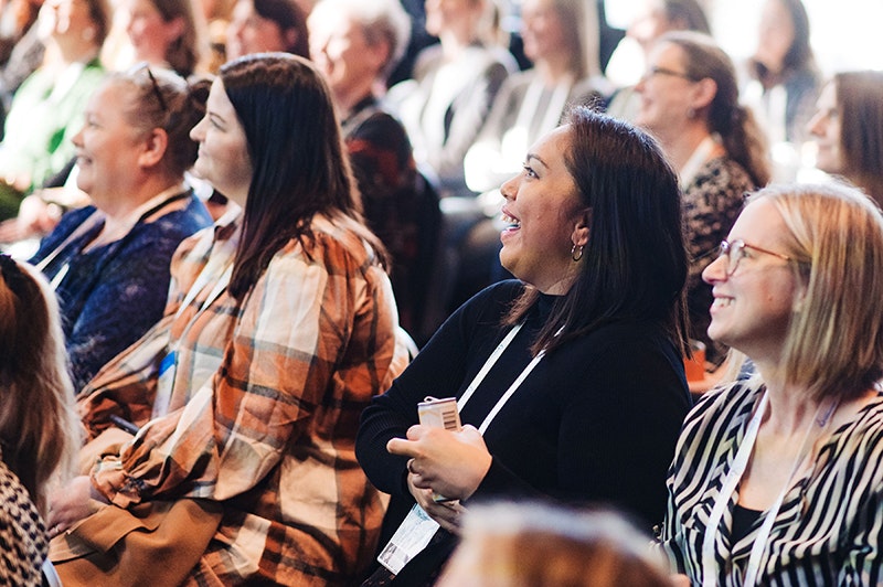 People in rows of chairs all laughing at something off camera.