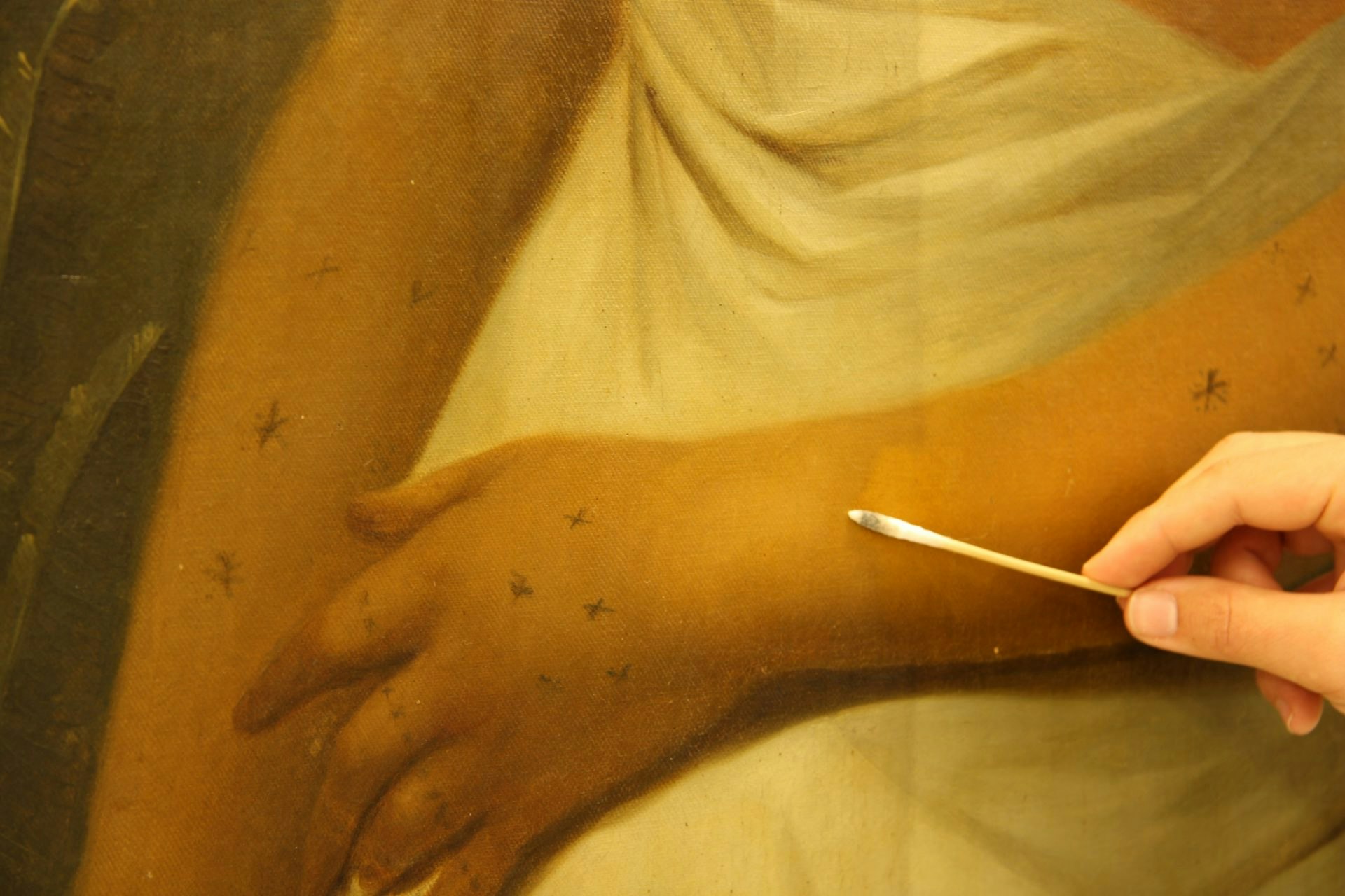 Close up of a conservator's hand holding a cotton bud against a painting.