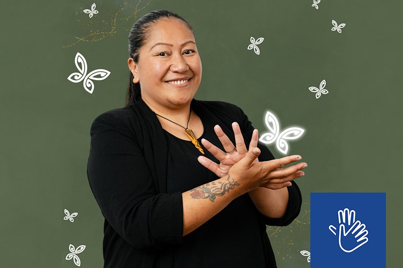 A woman is using her hands to say sign language and smiling at the camera.