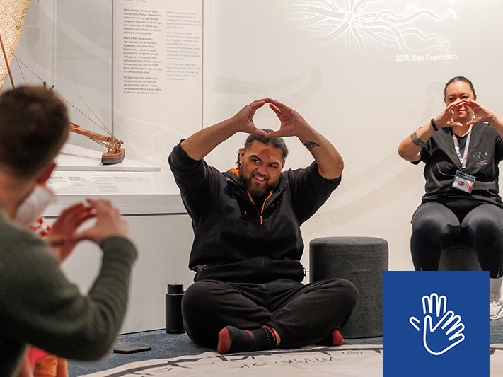 Matariki Whānau Day 2025 Te Papa. Photo by Jo Moore. Te Papa (268593) Two people are facing an audience sitting on the floor and holding their hands up in a circle shape.