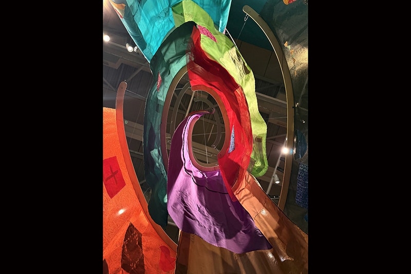 Looking up at a ceiling through several coloured banners hanging in a spiral.