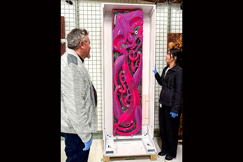 Two people are looking at a hot-pink carved panel.