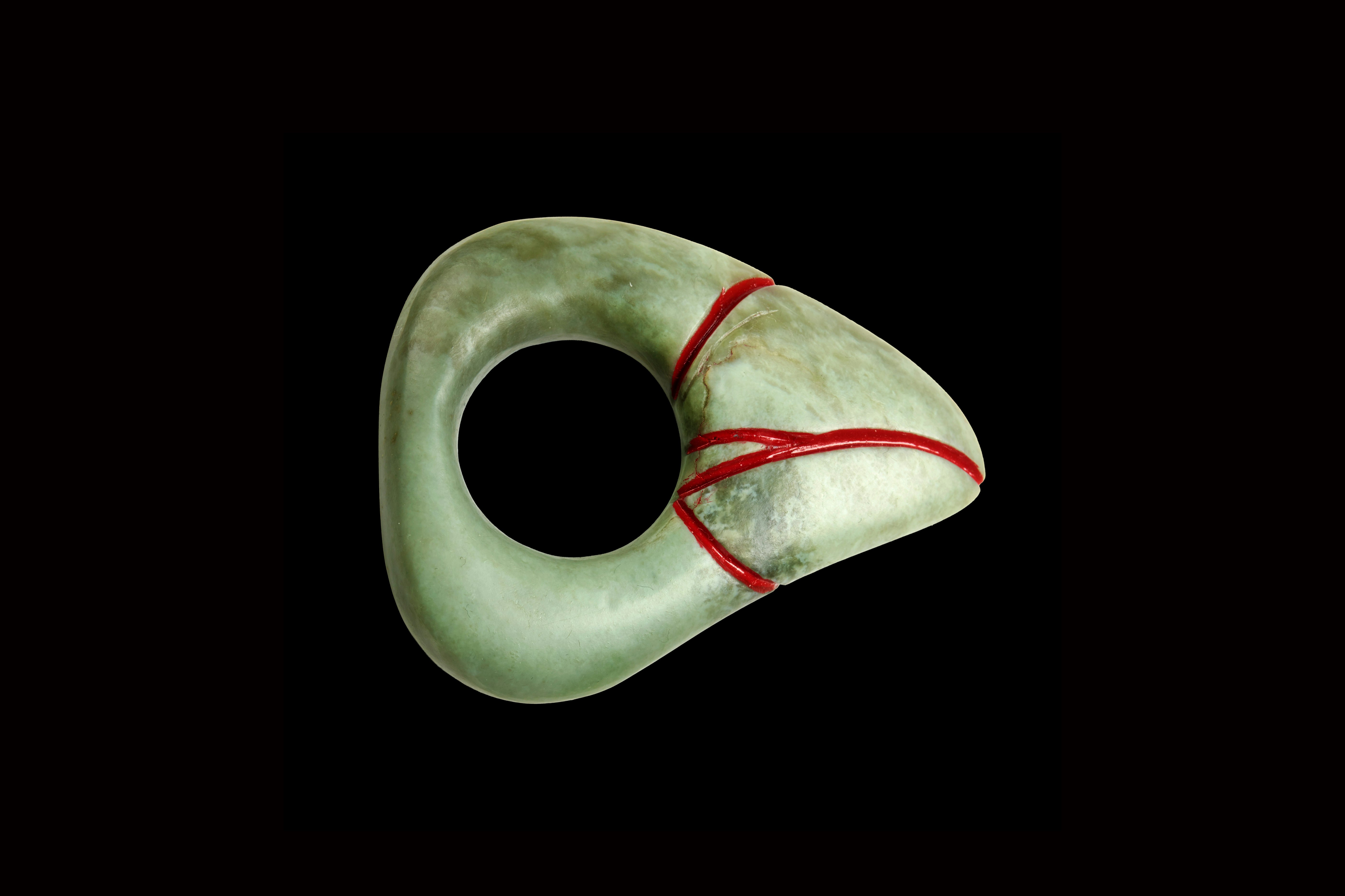 Pounamu ring in the shape of a triangle with a hole in the centre, and red-painted lines on the main corner.