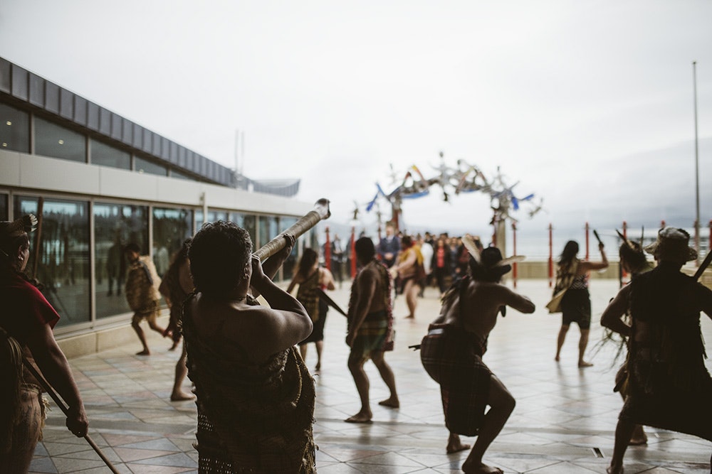 Silhouettes of people in Māori clothing challenging people who are walking onto the marae atea at a pōwhiri.