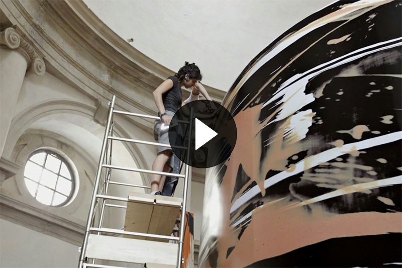 Two people are on some scaffolding installing a giant artwork in an old building.