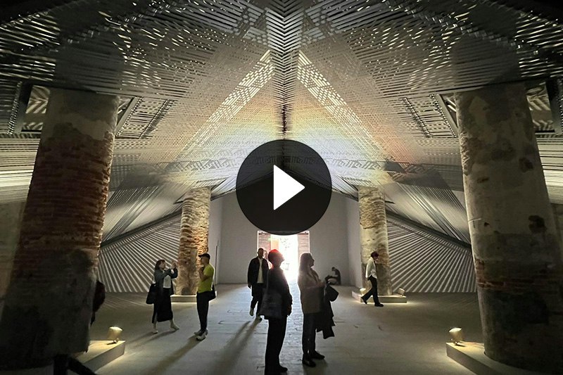 People standing in a large gallery with a weaving installation above them.