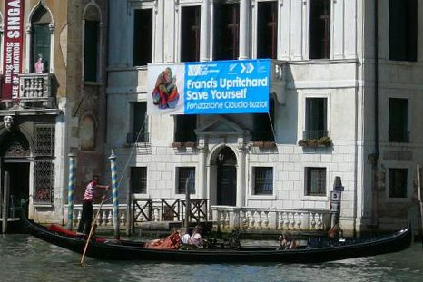 A gondola in Venice going in front of a building advertising Francis Upritchard's art installation.