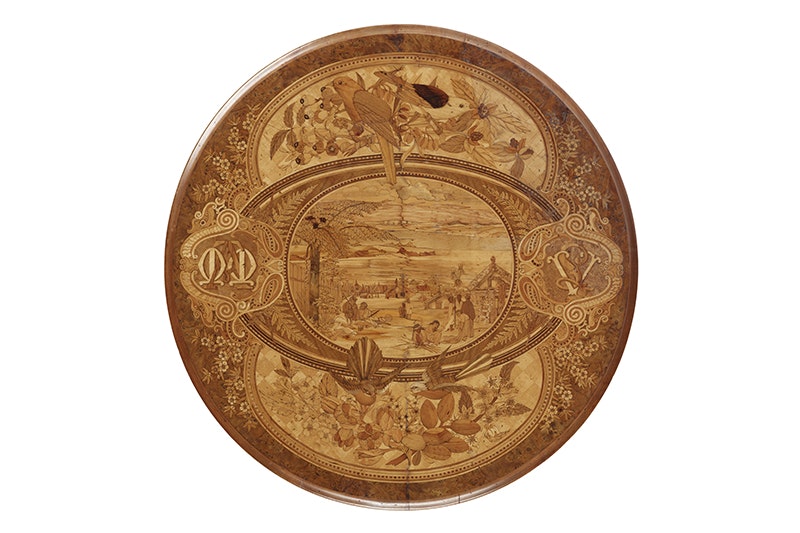 A wooden tabletop with nature and people scenes inlaid onto it.