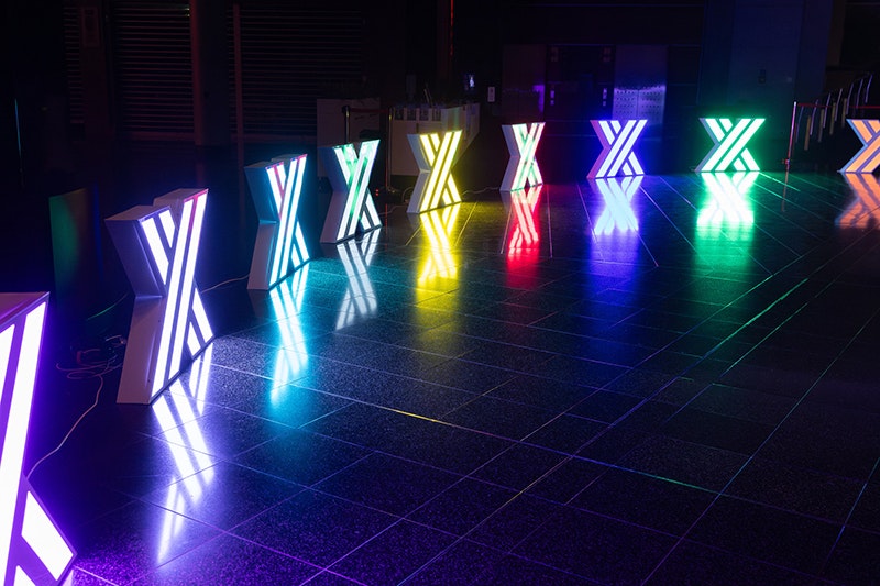 Nine lights each in the shape of an X arranged in an arc on a dark stage.