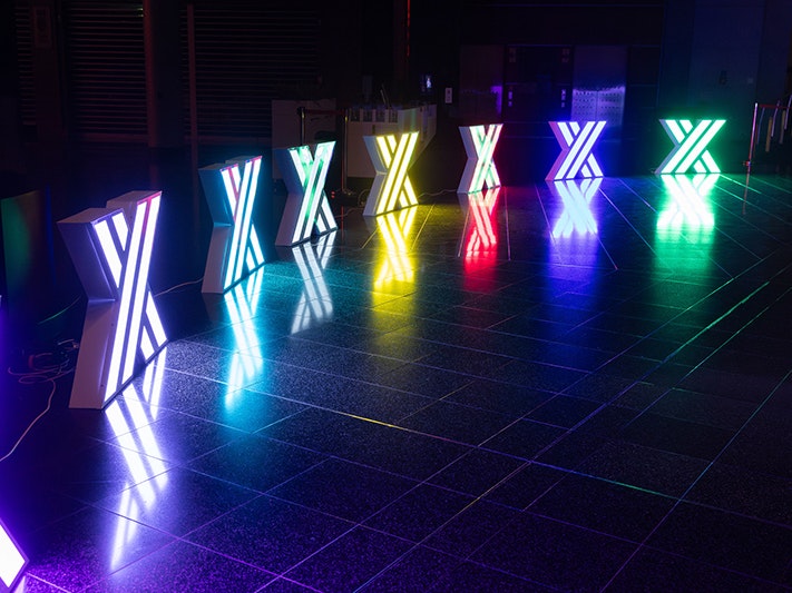 Matariki After Dark, 2025. Photo by Mel Waite. Te Papa (266480) Nine lights each in the shape of an X arranged in an arc on a dark stage.