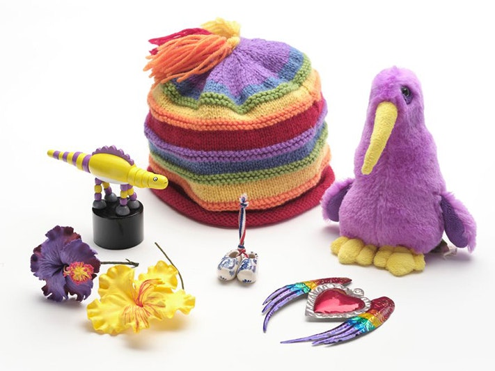 Travelling collection, various manufacturers. Gift of Mani Bruce Mitchell, 2023. Te Papa (GH026535/1-17) A selection of things that are purple and yellow including a hat, a kiwi, two fake flwers a dinosaur toy and a pressed-tin heart with wings.