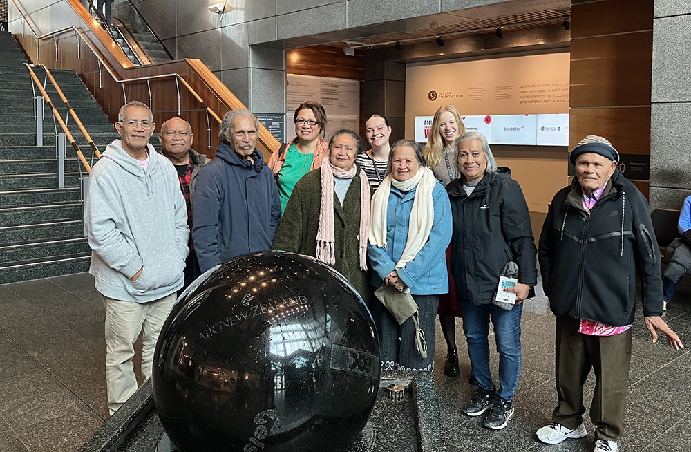 Ten people standing behind the large stone ball in the foyer of Te Papa. They are all smiling at the camera.