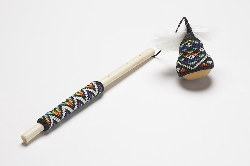 A small gourd with woven material covering it and it is attached to a stick that also has a woven handle.