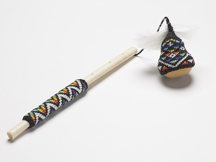 Te pū o Uenuku, Isaac Te Awa, weaver, New Zealand 2023. Purchased 2023. Te Papa (ME024544) A small gourd with woven material covering it and it is attached to a stick that also has a woven handle.
