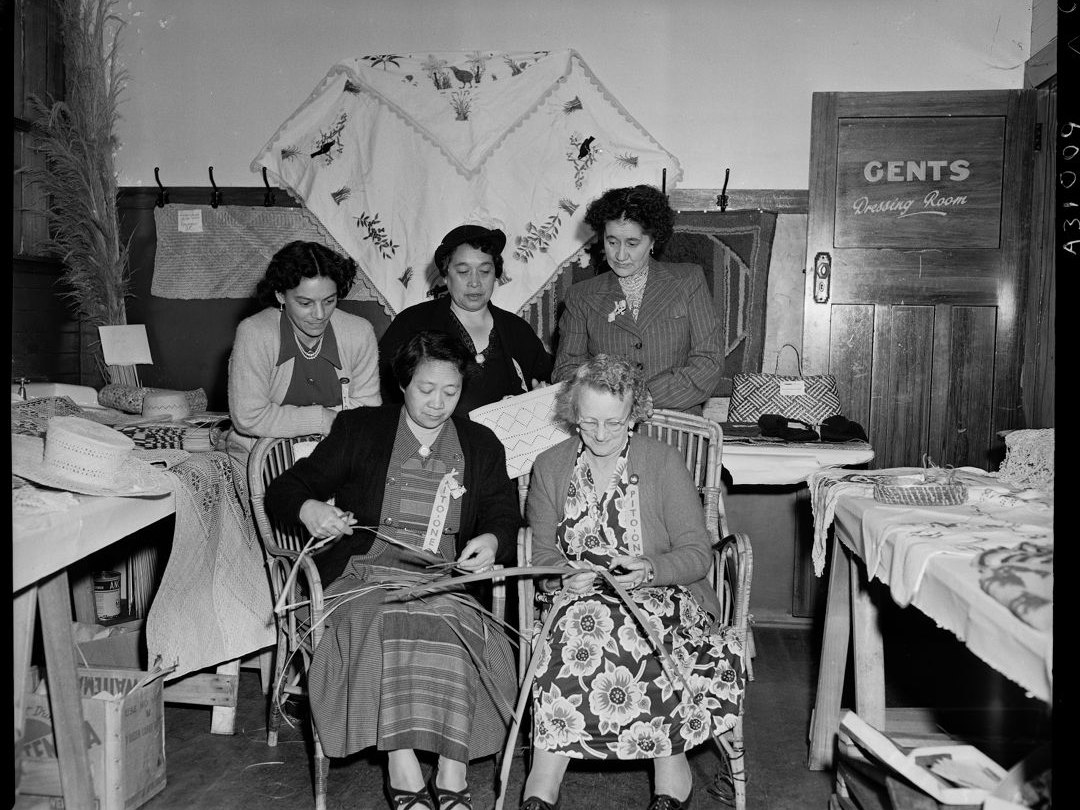 Mrs T Love demonstrating the art of flax weaving at the New Zealand Maori Women's Welfare League conference. Tourist and Publicity. Ref: 1/2-040546-F. Alexander Turnbull Library, Wellington, New Zealand. /records/23247934 Two women are sitting side by side weaving flax, while three other women look on.