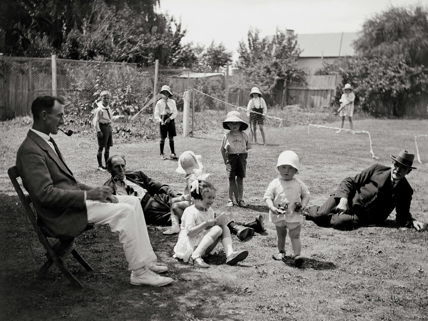 black and white photograph of men reclining on a lawn while children play