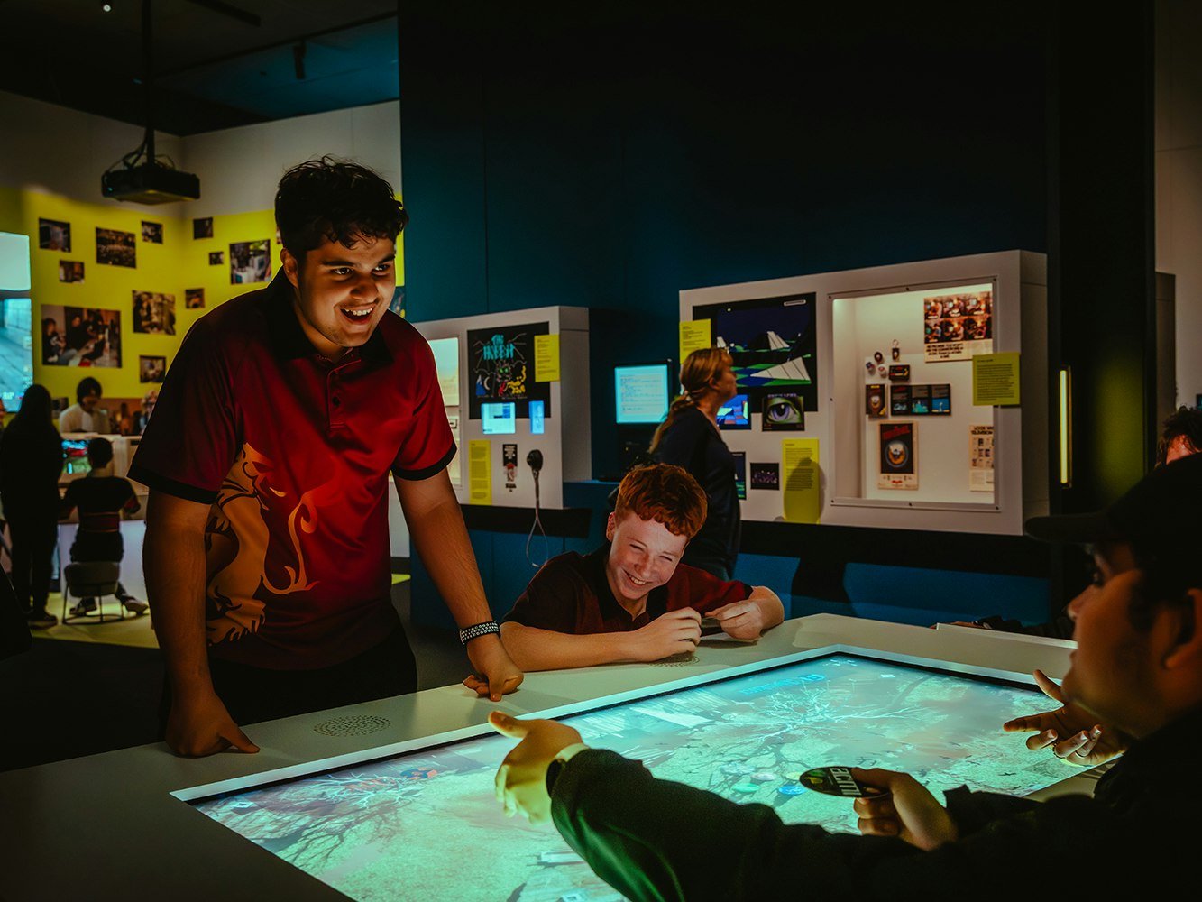 Game Worlds, 2025, ACMI. Photo © Matto Lucas. Several teenagers are playing a large video game and laughing at each other.