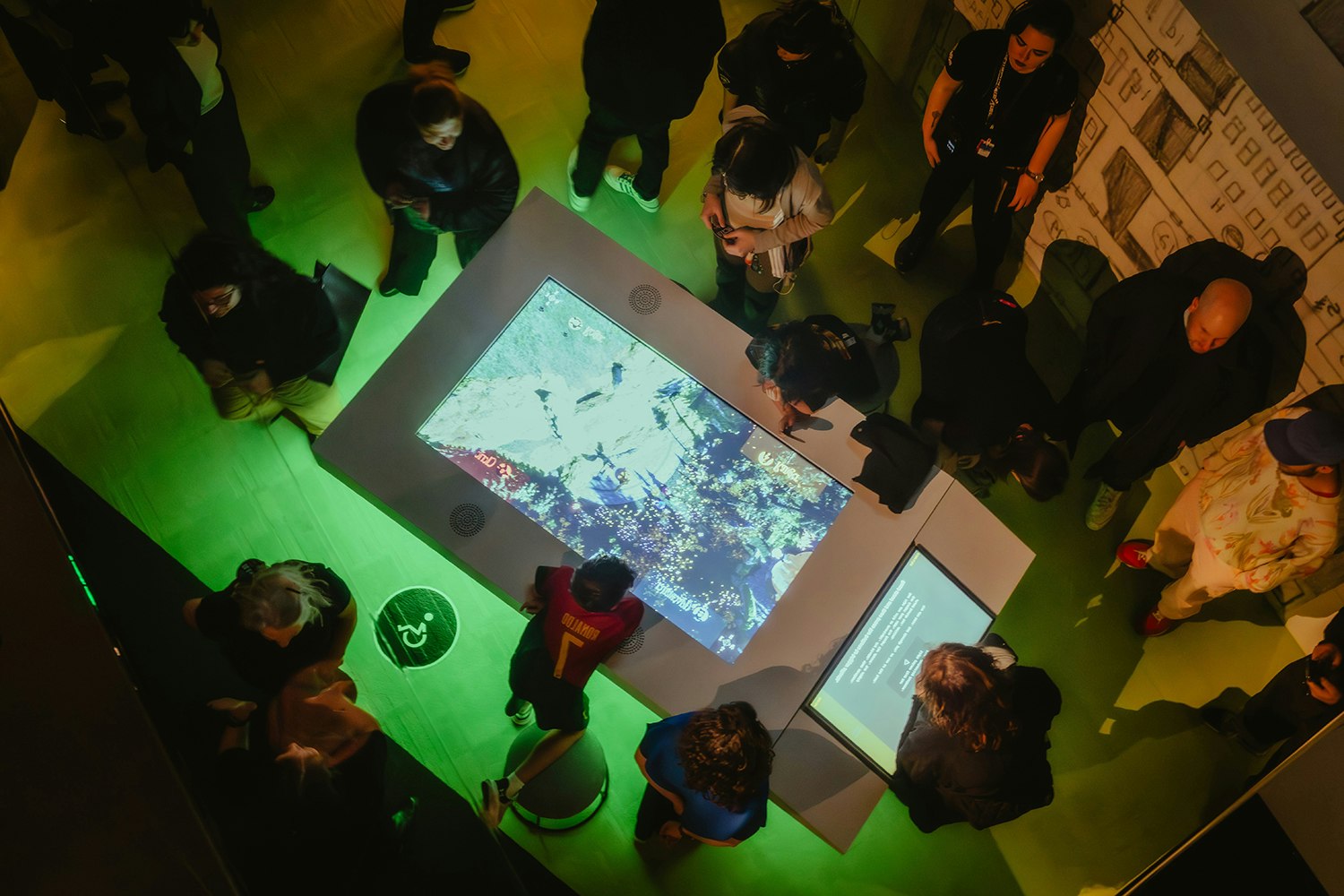 Several people are standing around a large touchscreen in a dimly lit room.