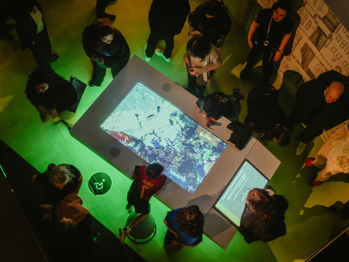 Game Worlds, ACMI, 2025. Photo © Matto Lucas Several people are standing around a large touchscreen in a dimly lit room.