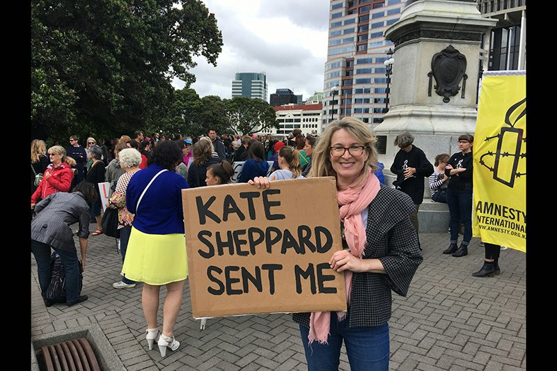 A woman is outside parliament and holding a sign saying "Kate Sheppard sent me"