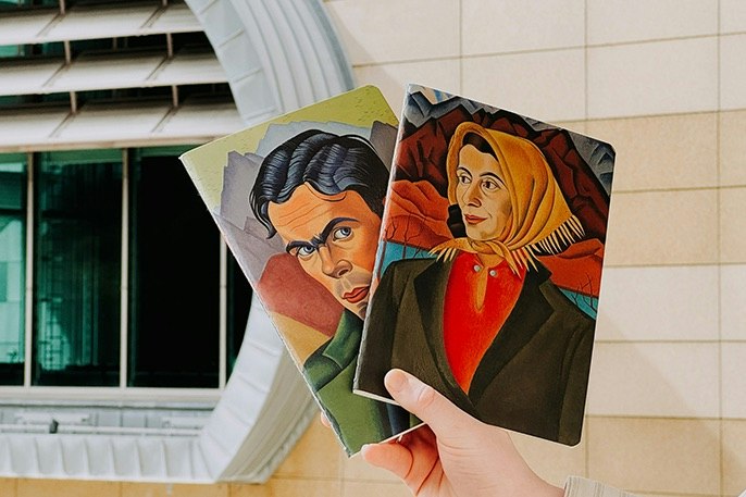A hand holding two notebooks with Rita Angus art on them.