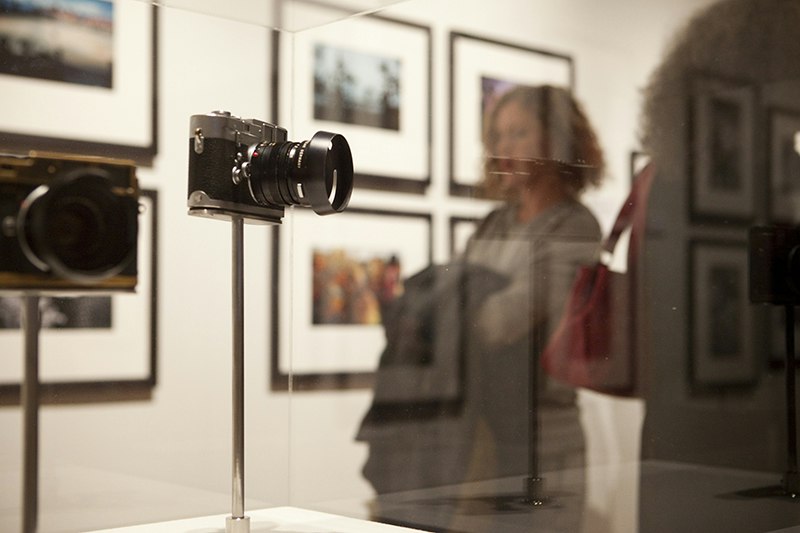A person is out of focus behind two cameras in a glass stand in a gallery.