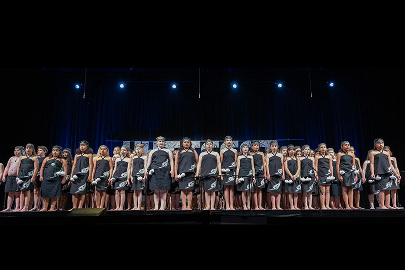 A line of intermediate school children on a stage. They are dressed in their Kapa Haka outfits.