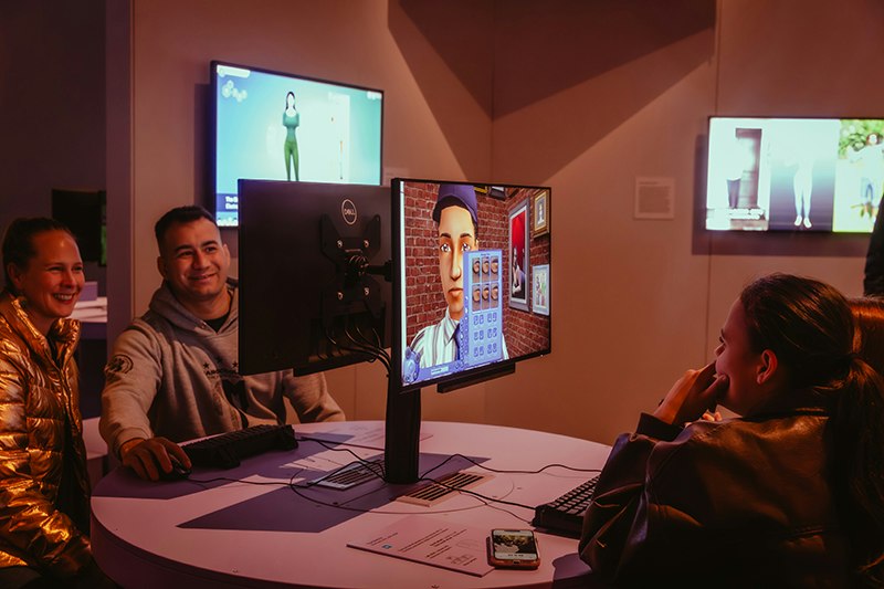 Three people are sitting in front of computer monitors playing games.