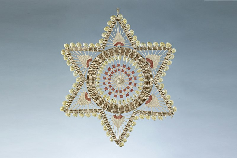 A wall hanging in the shape of a six-sided star made of sennit and shells.